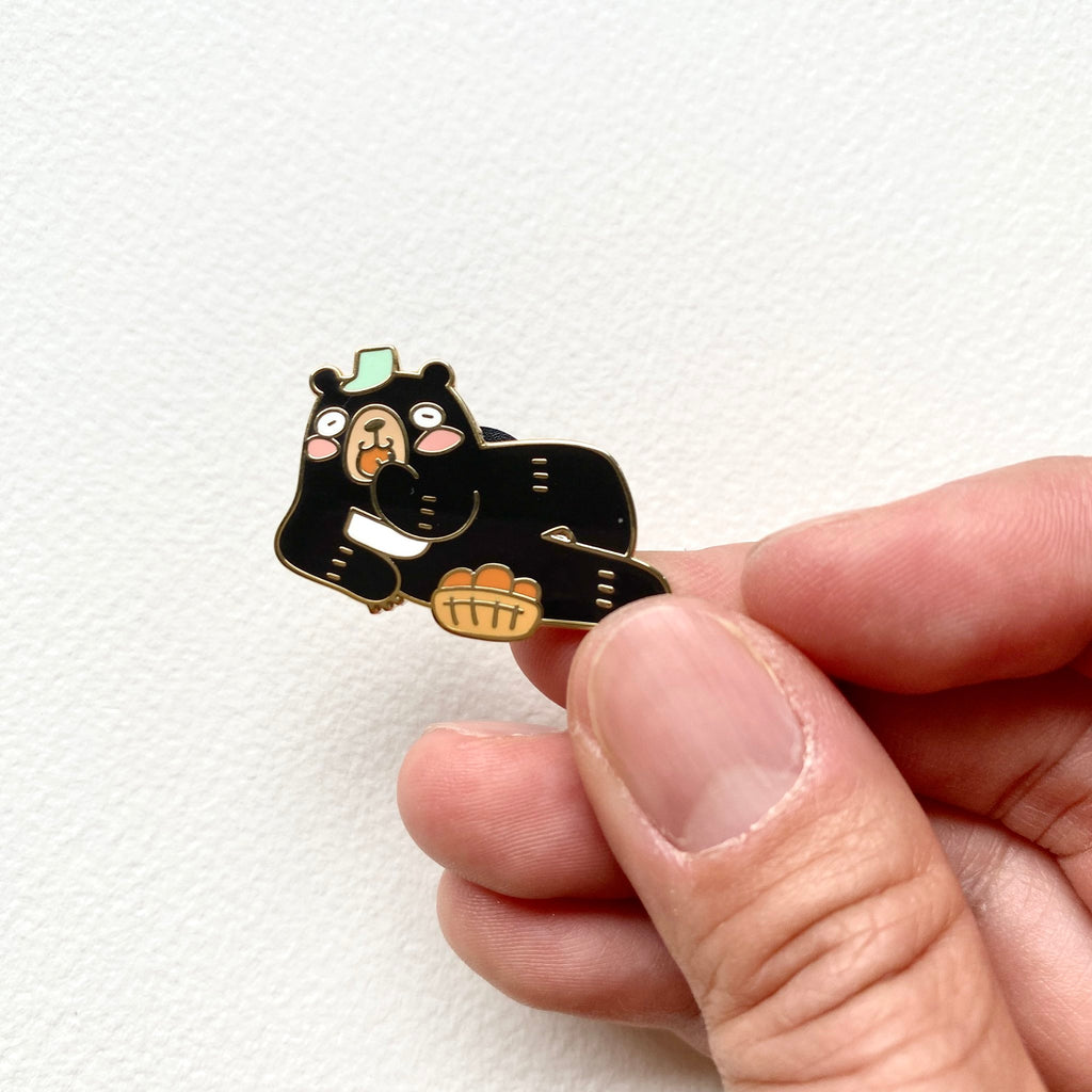 Principal Bear enamel pin held between two fingers to show how small it is