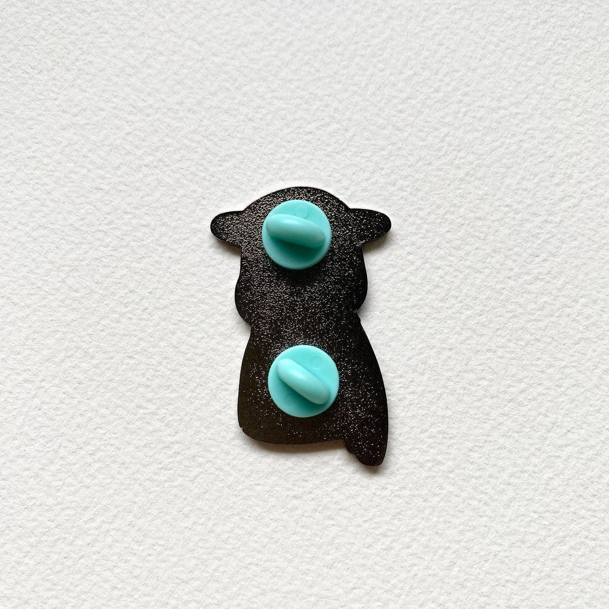 Back of the Mr. Otter enamel pin, black metal with two teal rubber pin backs