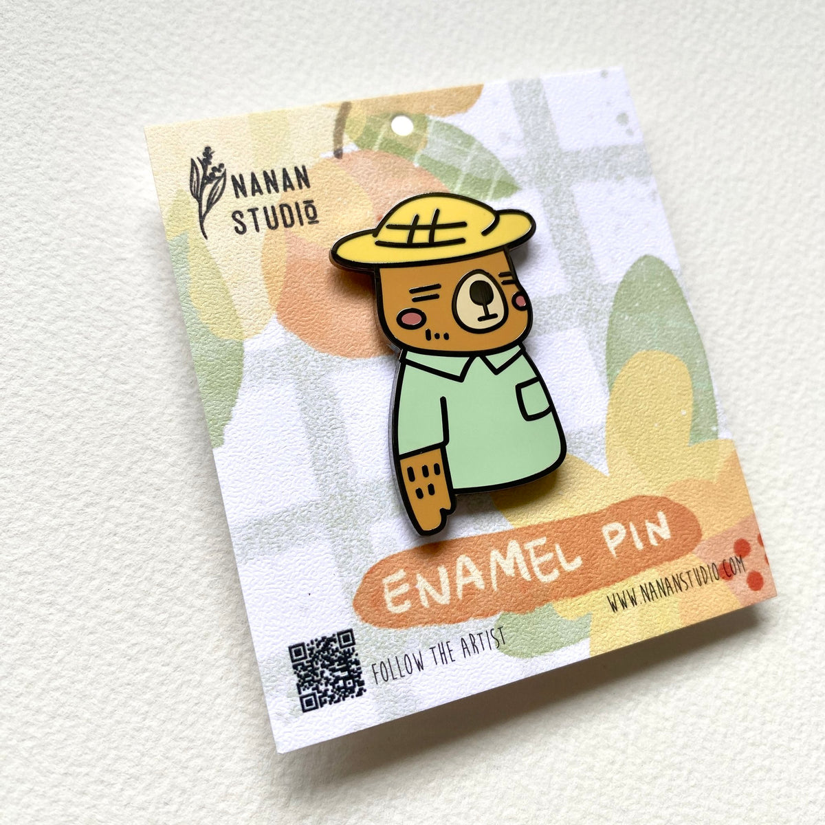 Mr. Otter enamel pin on its backing card, photographed at an angle to show the enamel shine