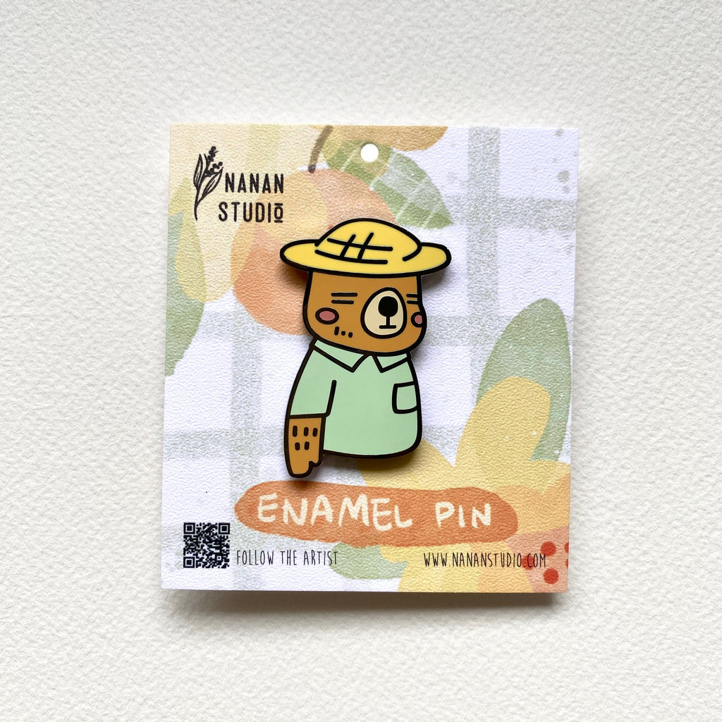 Mr. Otter enamel pin, an otter in a yellow straw hat and mint green shirt, on an illustrated Nanan Studio backing card