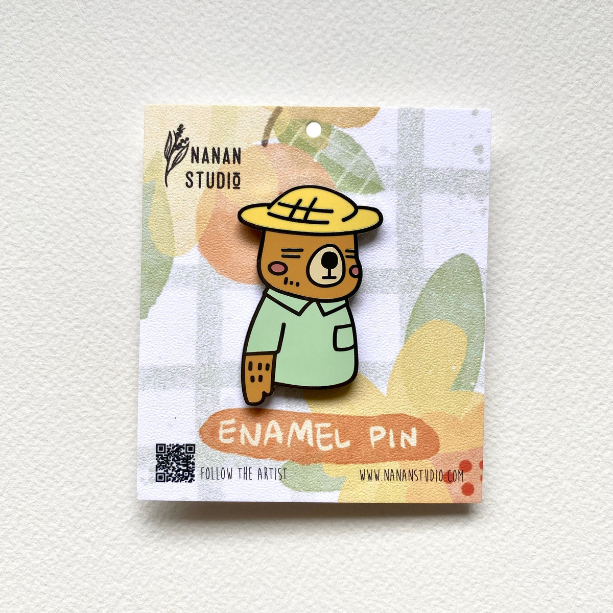 Mr. Otter enamel pin, an otter in a yellow straw hat and mint green shirt, on an illustrated Nanan Studio backing card