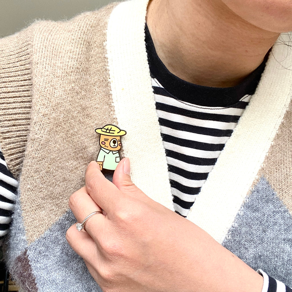 Mr. Otter enamel pin worn on the collar of a knitted vest, showing how small it is