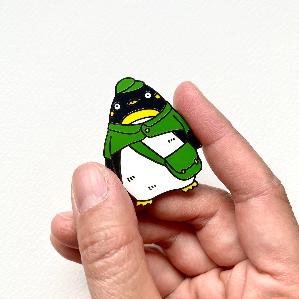 Penguin postman enamel pin held between two fingers to show its size