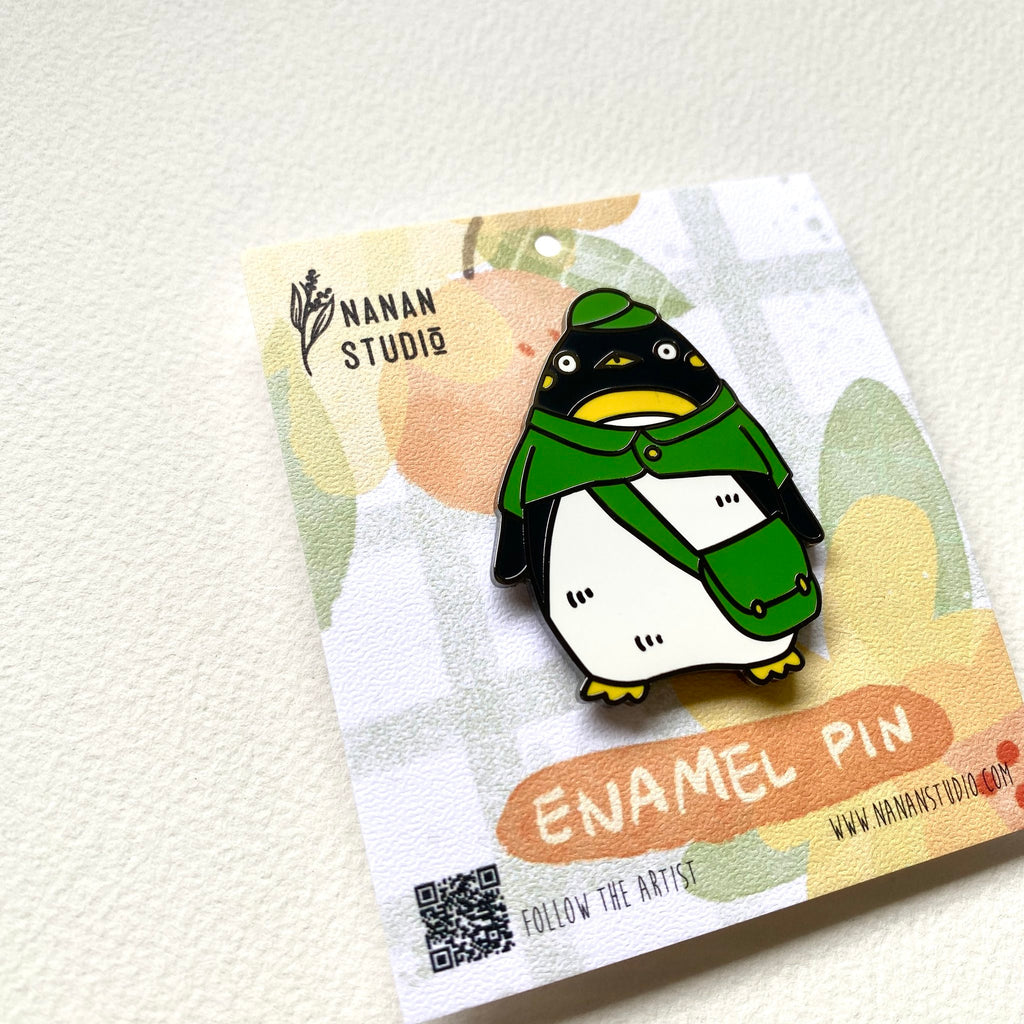 Penguin postman enamel pin on its backing card, tilted to show the Nanan Studio logo and QR code