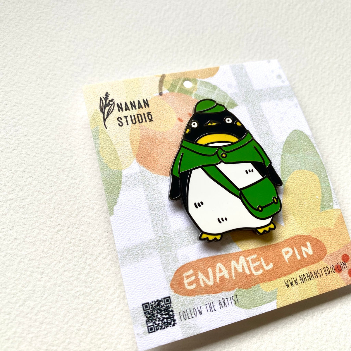 Penguin postman enamel pin on its backing card, tilted to show the Nanan Studio logo and QR code
