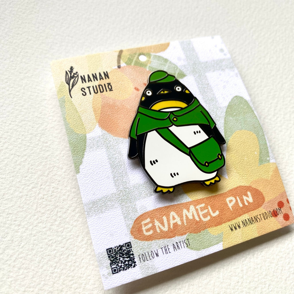 Penguin postman enamel pin on its backing card, photographed at an angle to show the enamel shine