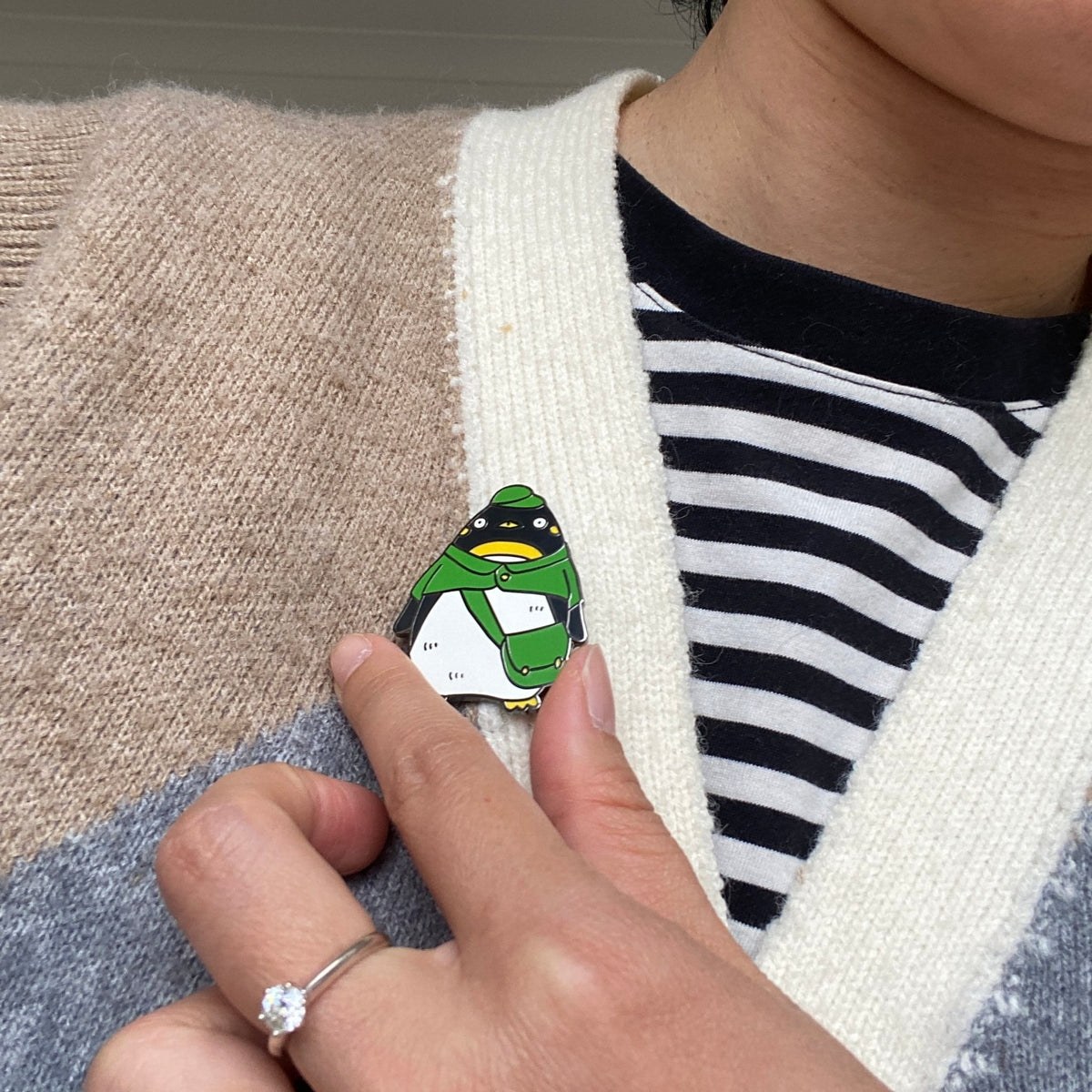 Penguin postman enamel pin worn on the front of a knitted vest
